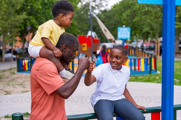African black ethnicity father waving with his children in the playground of the city park