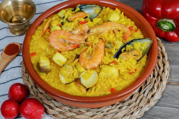 Appetizing typical spanish seafood paella in an earthenware casserole surrounded by some of its ingredients