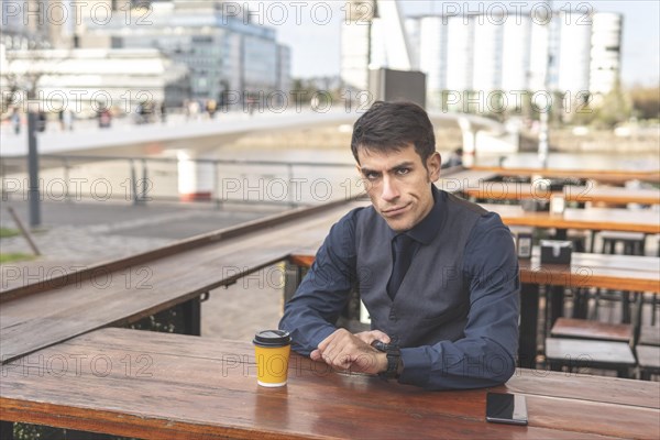 Business man sitting in a bar pointing at his watch looks disgusted at the camera. Delay concept