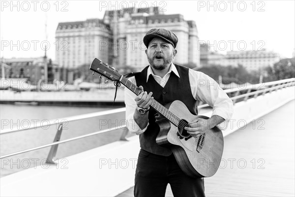 Black and white portrait of a musician playing the guitar and singing on a bridge over a river