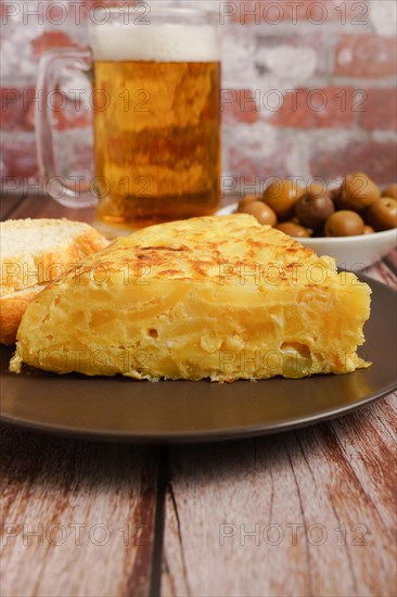 Typical spanish potato omelette freshly made on a wooden table with a fresh pitcher of beer