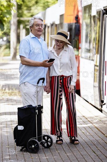 Elderly couple waiting for the tram at a stop with a smartphone in hand