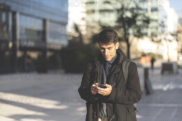 Portrait of businessman walking in the street texting with his phone