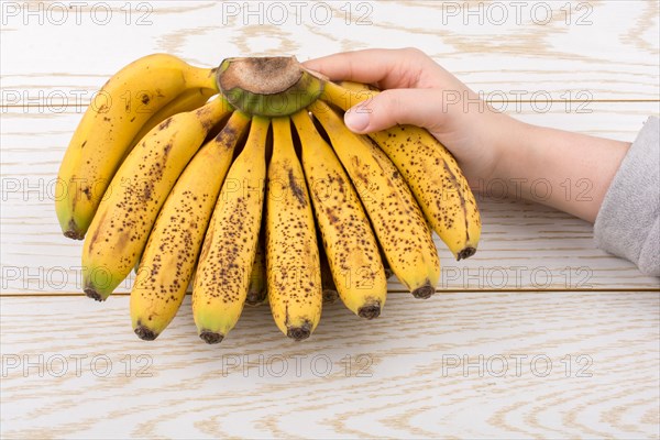 Hand holding bunch of freckled bananas on a wooden texture