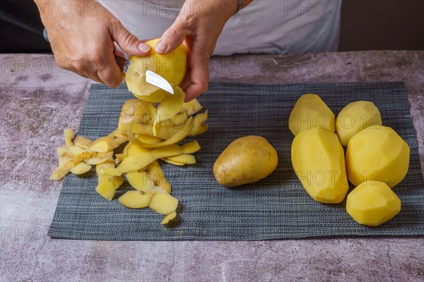 Close-up of a woman's hands in a white apron peeling potatoes with a knife