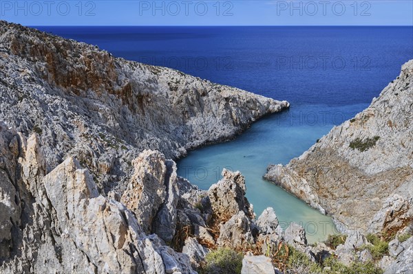 Vertical view of z-shaped cove or bay in typical summer Greek or Cretan landscape on sunny day. Great blue sky and beautiful clouds. Sharp limestone rocks in blurred foreground. Selective focus. Seitan Limania