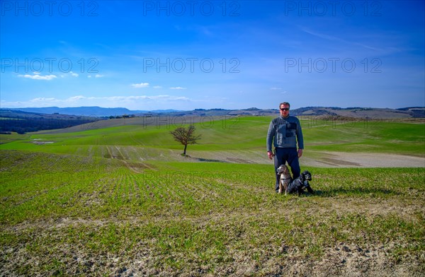 Man with Two Cocker Spaniel Dogs on the Beautiful Agriculture Landscape with a Single Tree in Tuscany