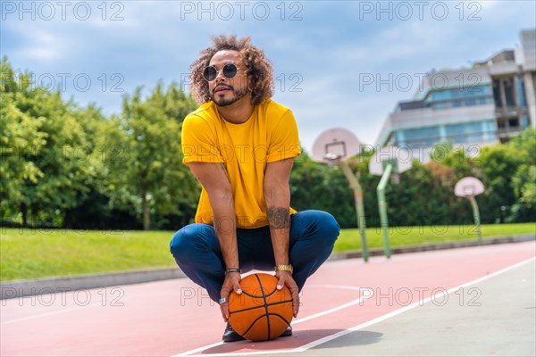 Portrait of an afro-haired man in a yellow t-shirt with a basketball ball. Portrait on a basketball court in the city