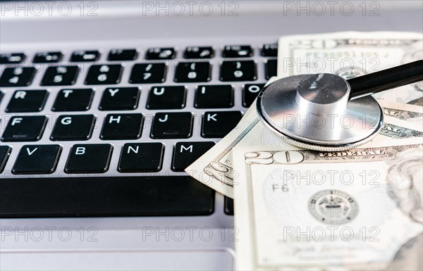 Stethoscope on dollar bills on top of laptop keyboard. Stethoscope on top of money on laptop keyboard