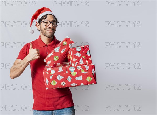 Christmas man holding gift boxes and smiling with thumb up. Smiling guy in christmas hat holding christmas gift boxes giving thumbs up. Friendly man in christmas clothes holding gift boxes