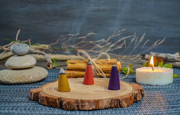 Colorful incense cones on a wooden disk with candles and zen stones stacked on top of them