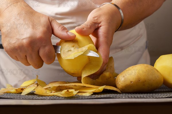 Close-up of a woman's hands in a white apron peeling potatoes with a knife