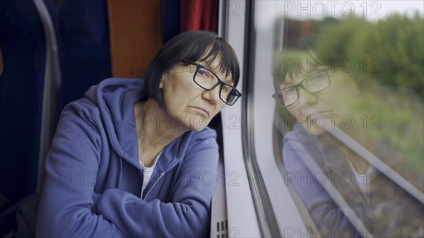 Elderly lady in glasses travels in train and looking out the window reflected in the glass