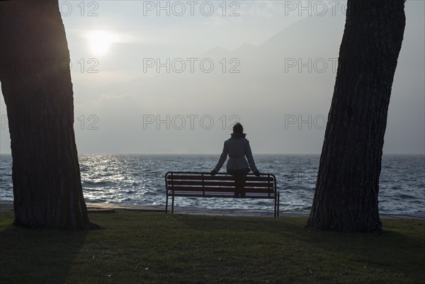 Woman Sitting on a Bench on the Waterfront Between Two Trees in Ascona