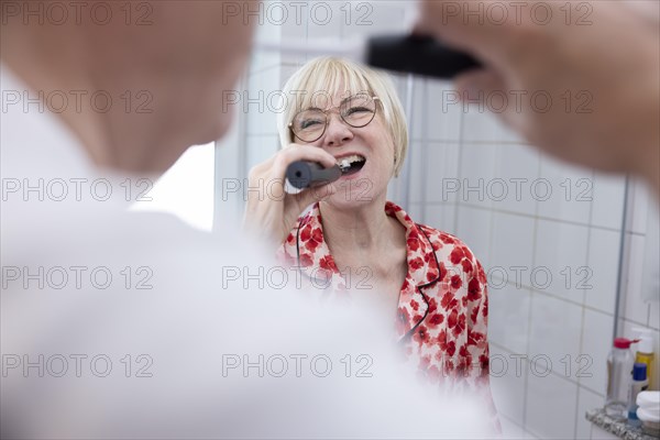 Elderly couple brush their teeth together in the bathroom