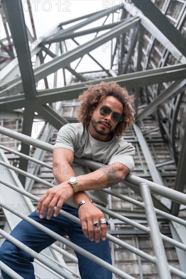 Portrait of a young man with afro hair wearing sunglasses on the stairs in the city