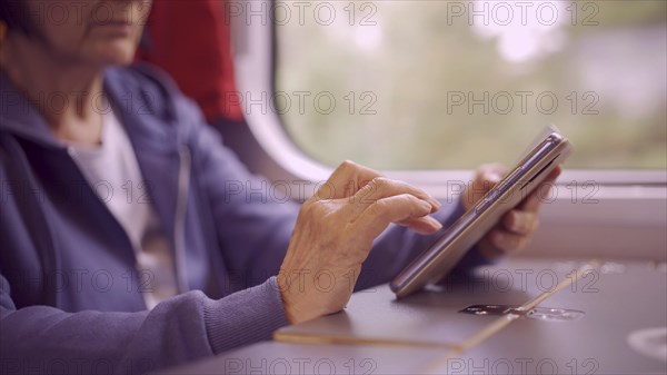 Close-up of the hands of a elderly lady sitting in a train carriageriage and using a smartphone