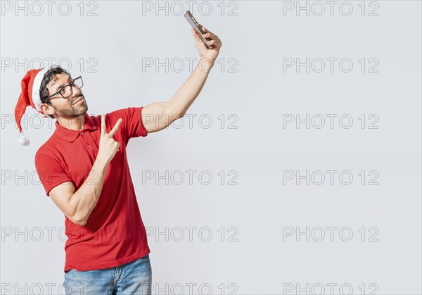 Smiling young man in christmas hat taking a selfie isolated. Happy handsome man in christmas hat taking a selfie. Happy guy taking a christmas selfie on isolated background
