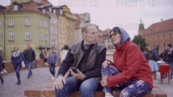 Elderly couple of tourists are sitting and talking in the historic center of an old European city