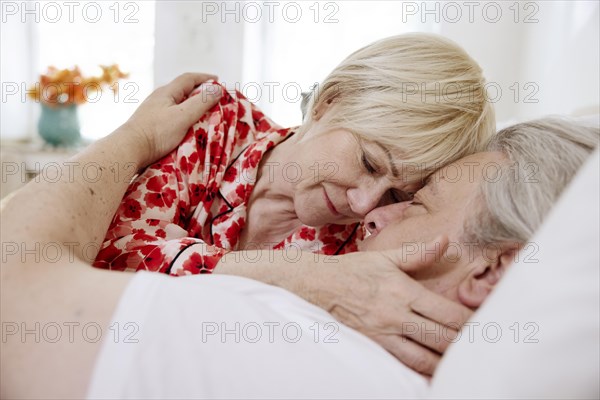 Elderly couple lying together in bed in bedroom embracing tenderly