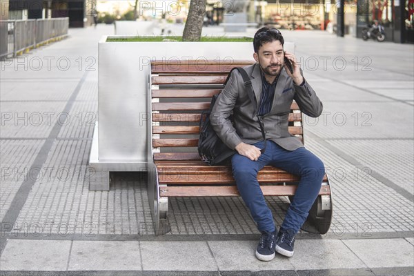 Latino businessman sitting on a bench talking on the phone