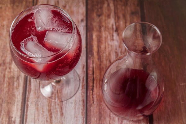 Top view of a sparkling glass of summer red wine on the rocks next to a decanter on a wooden table