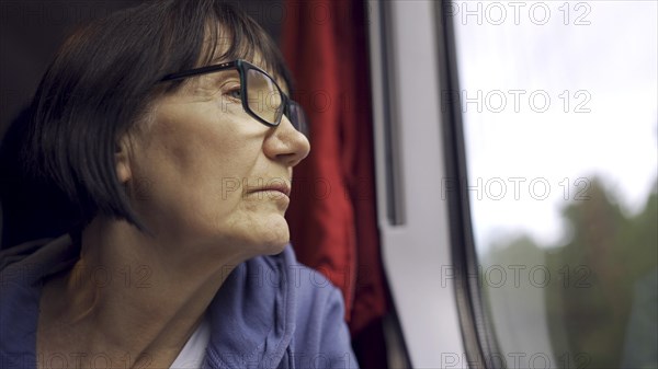 Elderly lady in glasses travels in train and looking out the window