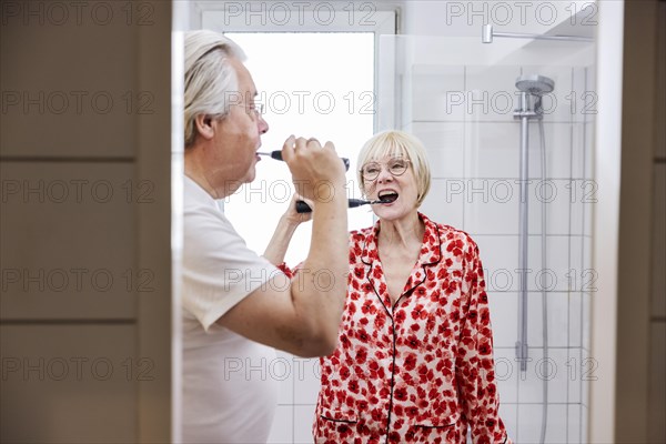 Elderly couple brush their teeth together in the bathroom