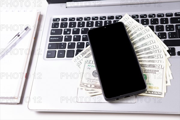 Mobile phone on top of dollar bills on laptop keyboard. Top view of laptop with cell phone and dollar bills. Cell phone on laptop keyboard and dollar bills