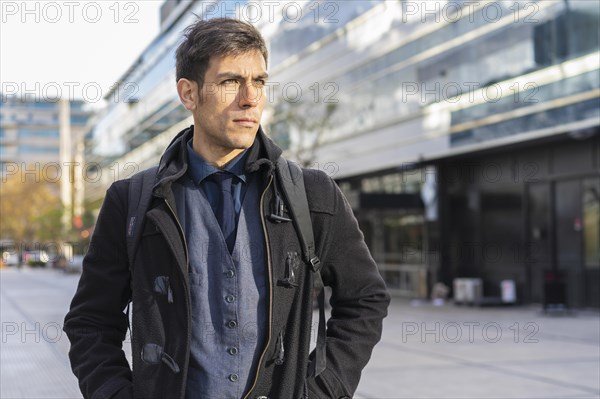 An attractive businessman with his backpack on looking away near his office