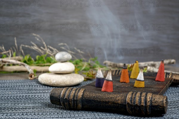 Colorful incense cones burning and smoking on a wooden tray with stacked zen stones