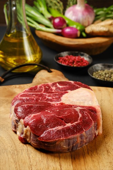 Closeup view of raw beef shank cross-cut on chopping board with ingredients for cooking