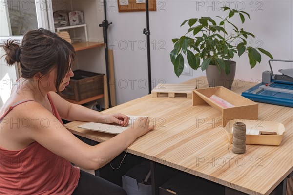 Young brunette girl with long hair craftswoman working on her products in her home workshop sewing notebooks