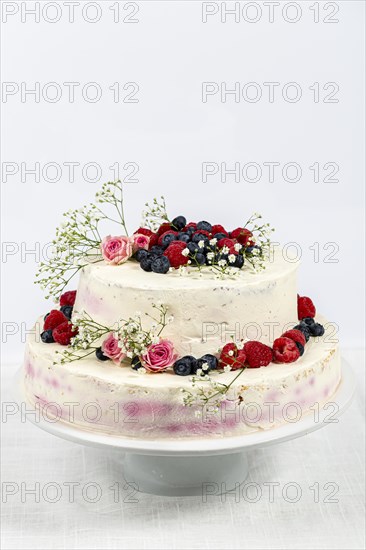 Summery fresh two tier wedding cake decorated with berries and flowers festive cream cake on light background