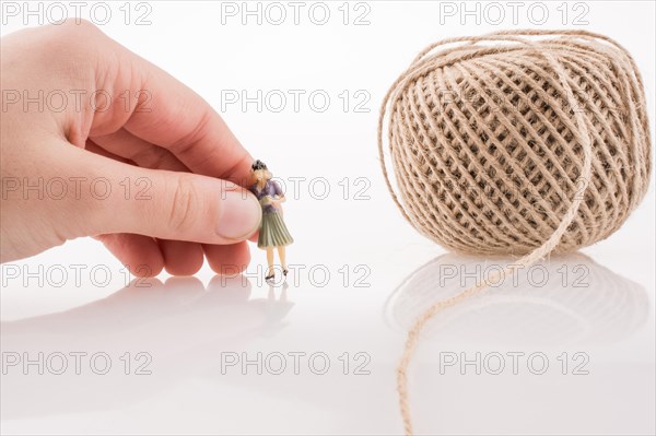 Woman figure beside a linen spool of thread on a white background