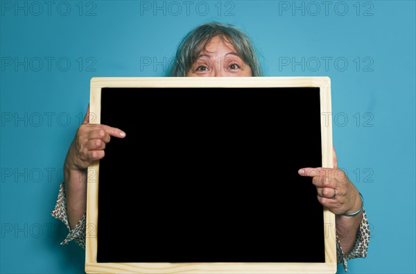 Older white-haired woman holding a blackboard with space for copying text
