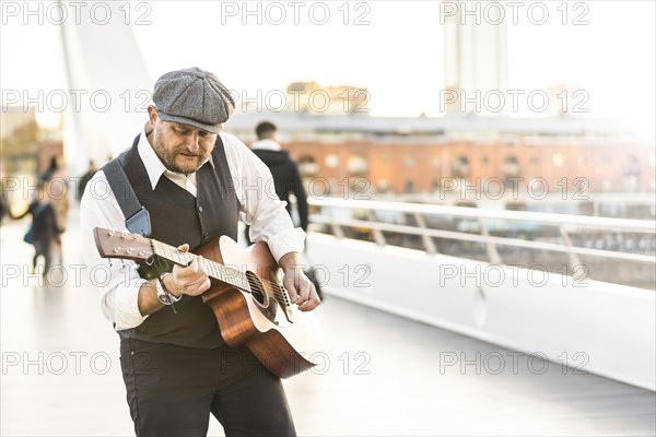A street musician performing songs on his guitar and singing as people walk by