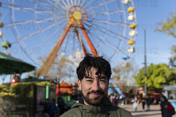 Portrait of latino man in an amusement park posing happy with the ferris wheel in the background