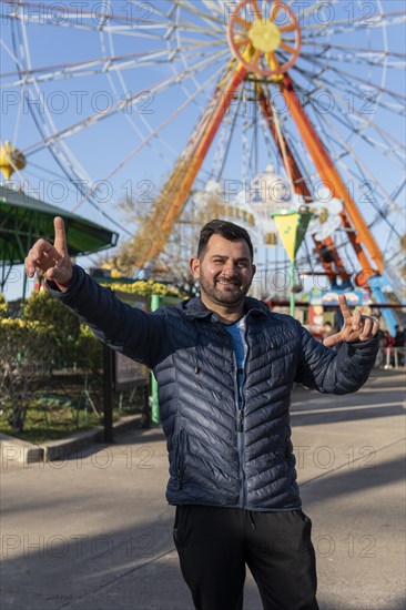 Portrait of latino man in an amusement park posing happy with the ferris wheel in the background