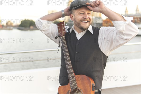 Guitarist posing on a bridge over a river with his guitar