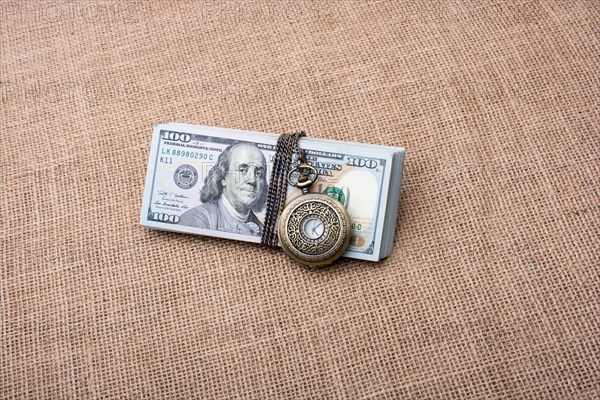 Pocket watch wrapped around banknote bundle of US dollar