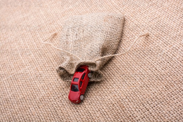 Red toy car coming out of a linen sack on a linen canvas