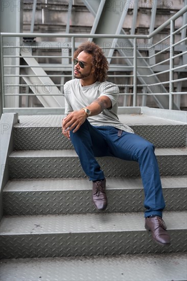 Portrait of a young man with afro hair wearing sunglasses on the stairs in the city sitting