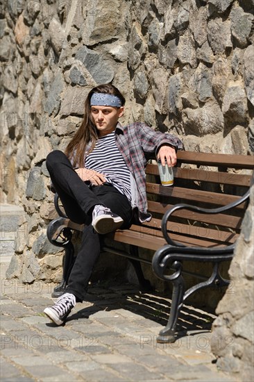 Long haired man sitting on bench with glass of drink in a sunny day