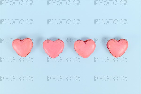 Heart shaped French macaron sweets in a row on blue background