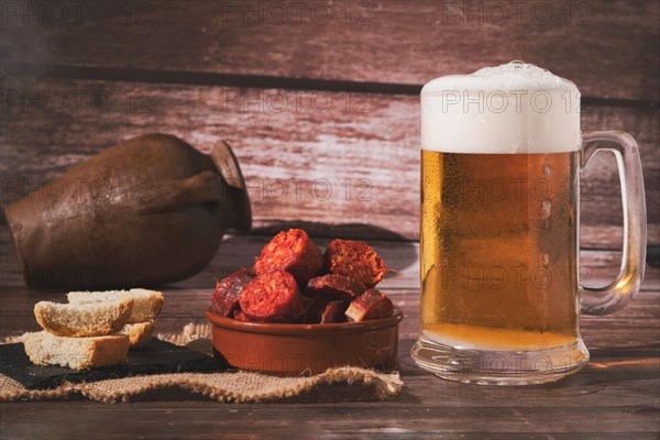 Mug of fresh beer with foam and clay pot with bread and chorizo sausage