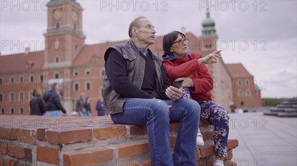 Elderly couple of tourists are sitting and talking in the historic center of an old European city