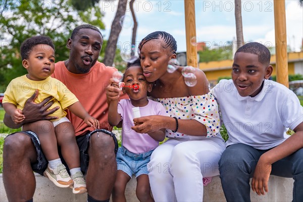 African black ethnic family with children in playground blowing soap bubbles