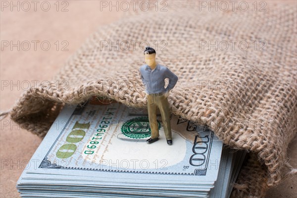 Man figurine standing on bundle of US dollar in a sack
