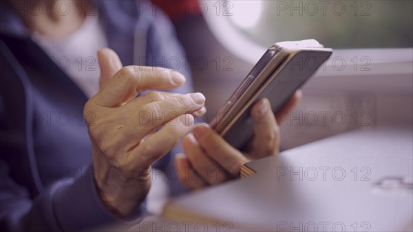 Close-up of the hands of a elderly lady sitting in a train carriageriage and using a smartphone